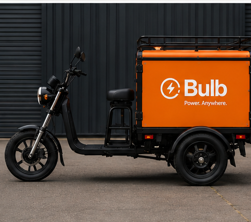 The Bulb power trike, an orange-and-black electric three-wheeler whose cargo box opens into a full power unit with fans, a breaker panel, outlets and a battery pack.